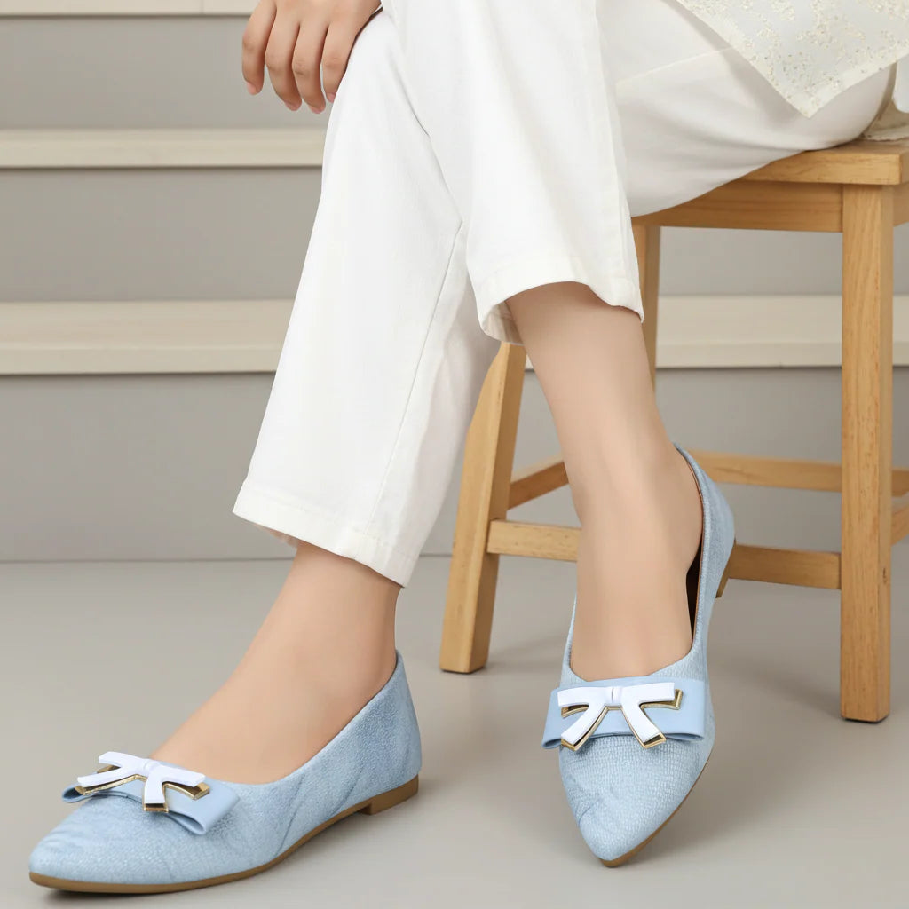 Light blue shoes with white bows worn by a person sitting on a wooden stool.