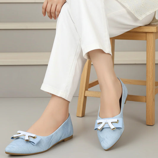 Light blue shoes with white bows worn by a person sitting on a wooden stool.
